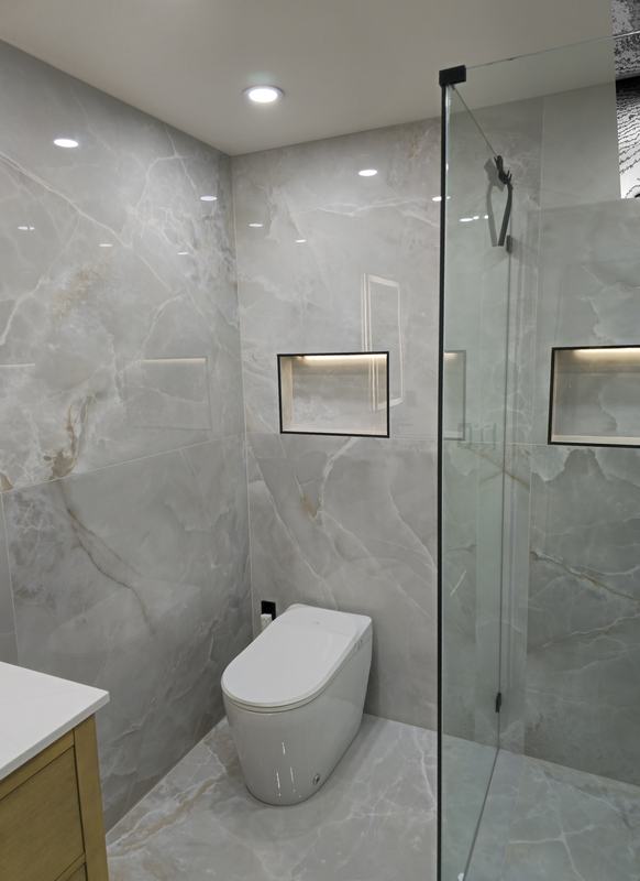 Finished shower with marble-look tile, lit niches and a glass panel